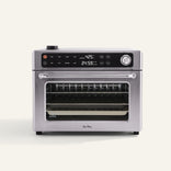 A stainless steel countertop oven with digital controls, a clear front door, and a visible wire rack inside, set against a plain background.