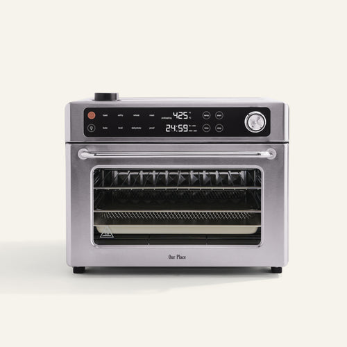 A stainless steel countertop oven with digital controls, a clear front door, and a visible wire rack inside, set against a plain background.