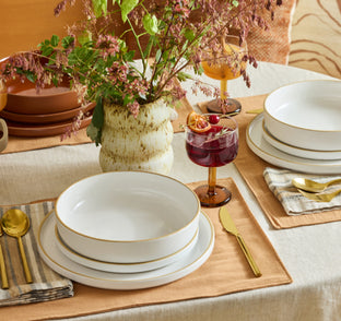 Dining table setting with white ceramic plates, gold cutlery, and a vase of flowers.