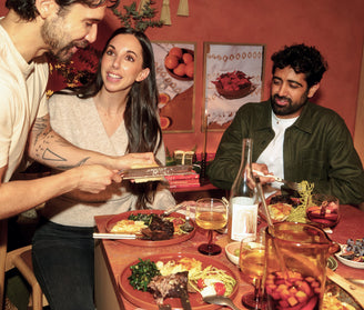 Three people sitting around a table with a meal, including a bottle of wine and various dishes.