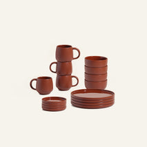 The Dinnerware Set includes stacked brown ceramic mugs, bowls, small plates, and large plates, all displayed against a plain light background.
