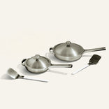 Set of stainless steel cookware including pots, pans, and spatulas on a white background