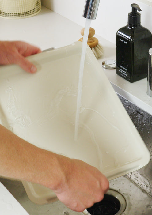 Person washing a cutting board under running water in a sink.